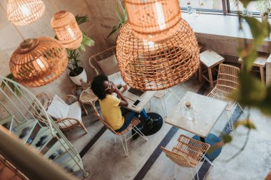 Kafeteryada dijital aletlerle çalışan genç Afrikalı bir kadın.