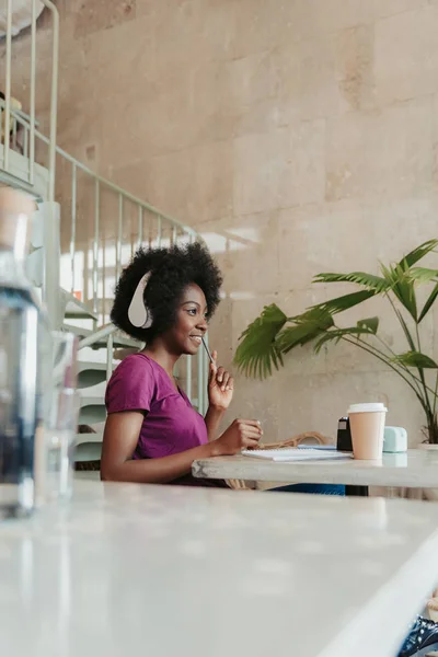 Vista lateral de mujer africana en auriculares disfrutando del tiempo en la cafetería — Foto de Stock