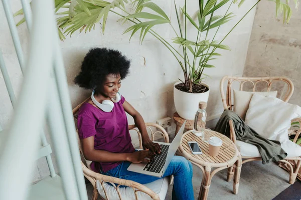 Glückliche Afrikanerin mit Kopfhörern auf den Schultern surft im Internet im Café — Stockfoto