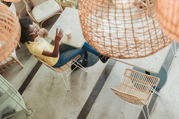 Shocked African woman keeping smartphone in arms while sitting at table — Stock Photo, Image