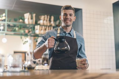 Kahve tutarken kameraya gülümseyen dost barista