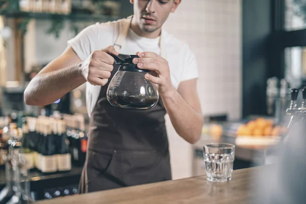 Zorgvuldige Barista kijkend naar de glazen koffiekan in zijn handen — Stockfoto