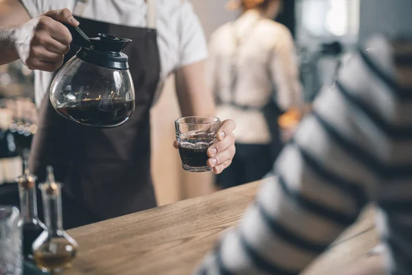 Close up of coffee jug and glass in hands of barista