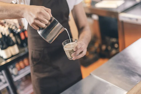 Barista holding milk pitcher while making coffee with milk