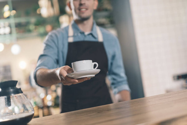Selective focus of cup on the plate in hand of barista