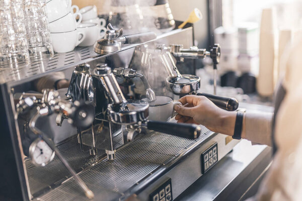 Hand of barista holding white cup and adding hot water into it