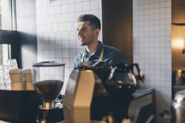 Neşeli barista kahve değirmeni önünde duran ve gülümseyen