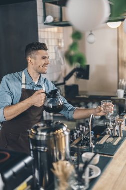 Boş cam ve kahve sürahi tutarken gülümseyen dostu barista