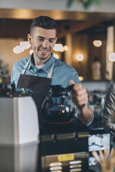 コーヒーマシンにコーヒージャグを置く笑顔のバリスタのクローズアップ — ストック写真