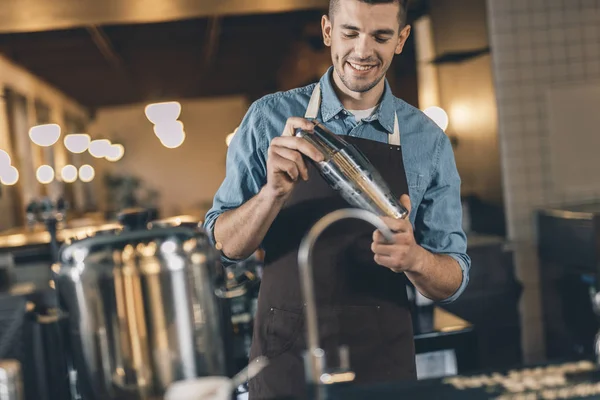 Jonge lachende barman met cocktailshaker aan het werk — Stockfoto