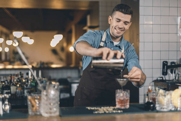 Happy bartender pouring cocktail and smiling cheerfully