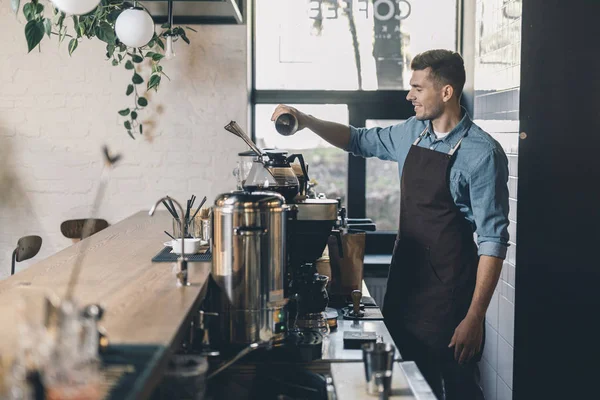 Jeune barista tamiser le café dans le réservoir de grain et sourire — Photo