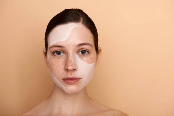 Gyönyörű fiatal nő, fehér arc maszk áll szemben bézs háttér — Stock Fotó