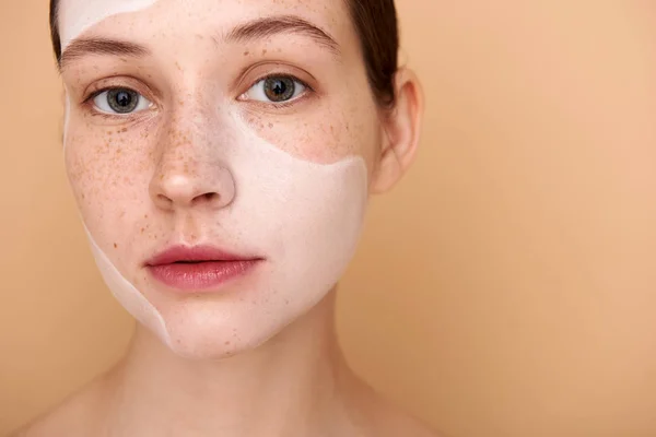Красива молода жінка з веснянками використовує білу маску для обличчя — стокове фото