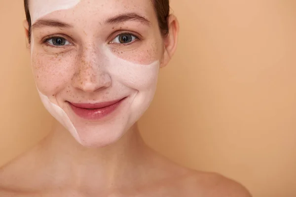 Carino sorridente ragazza con maschera bianca sul viso in piedi contro sfondo beige — Foto Stock