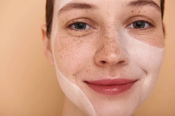 Söt tjej med vit mask på hennes ansikte stående mot beige bakgrund — Stockfoto