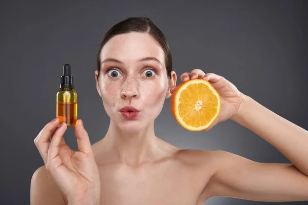 Mulher jovem bonito com sardas segurando laranja e soro de vitamina para o rosto — Fotografia de Stock