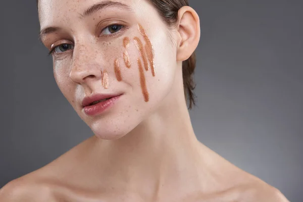 Linda chica con brillo de labios de oro en su cara posando sobre fondo gris — Foto de Stock