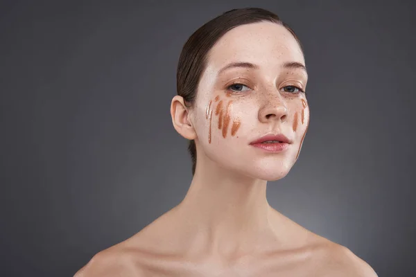 Mooi meisje met gouden lip gloss op haar gezicht poseren tegen grijze achtergrond — Stockfoto