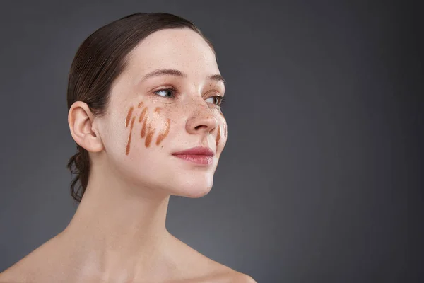 Schattig meisje met gouden lip gloss op haar gezicht staande tegen grijze achtergrond — Stockfoto