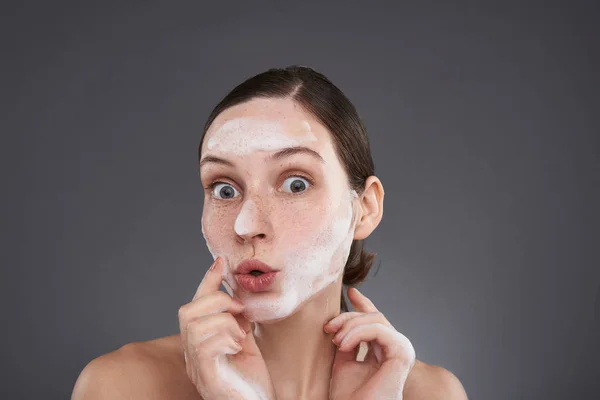 Bonita chica con pecas haciendo pucheros labios y lavándose la cara con jabones — Foto de Stock
