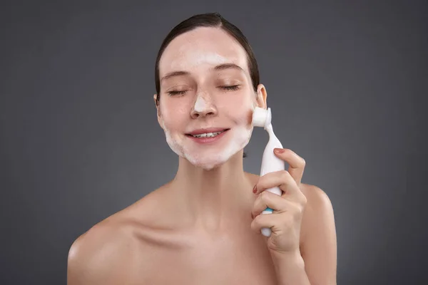 Chica bonita con los ojos cerrados usando cepillo de limpieza de poros después del baño —  Fotos de Stock