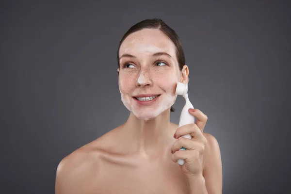 Linda chica sonriente usando cepillo de limpieza de poros después del baño —  Fotos de Stock