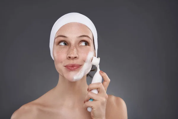 Affascinante ragazza in fascia bianca utilizzando spazzola detergente poro dopo il bagno — Foto Stock