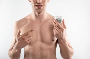 Mükemmel vücutlu genç adam kozmetik krem kavanozunu tutuyor ve onu işaret ediyor.