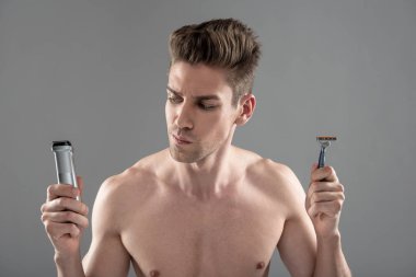 Yakışıklı genç adam tıraş makinesi ve tek kullanımlık jilet arasında seçim