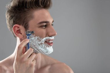 Tek kullanımlık jiletle tıraş gülen genç adam