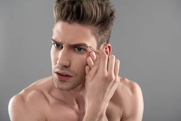 Joven guapo con rastrojo arrancando cejas con pinzas — Foto de Stock