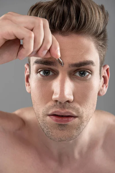 Jovem bonito com corte de cabelo elegante arrancando sobrancelhas com pinças — Fotografia de Stock