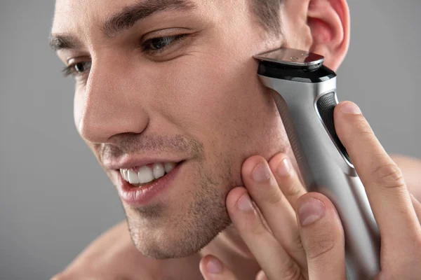 Joyful young man shaving with electric razor — Stock Photo, Image