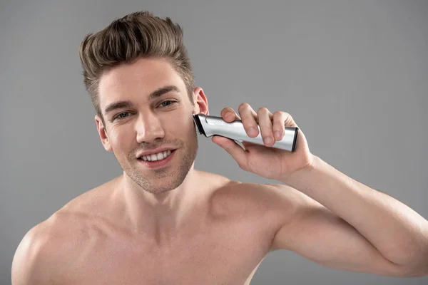 Smiling young man shaving with electric razor — Stock Photo, Image