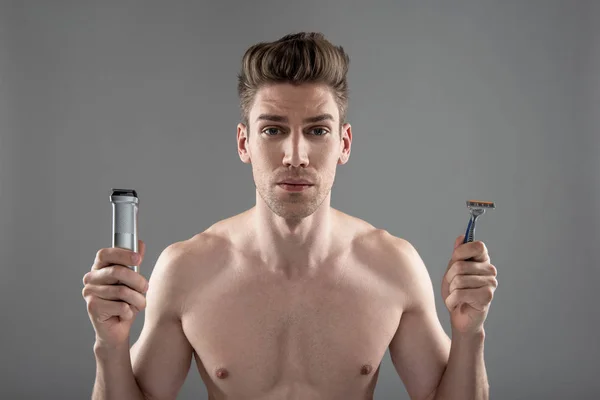 Όμορφος νέος άνθρωπος κρατώντας ηλεκτρική ξυριστική μηχανή και μίας χρήσης ξυριστική μηχανή — Φωτογραφία Αρχείου