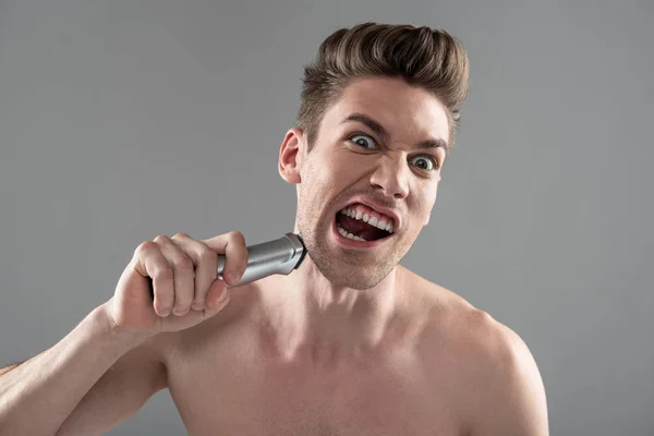 Irritado jovem barbear com lâmina elétrica e gritando — Fotografia de Stock