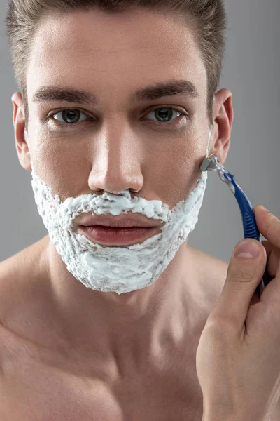 Привлекательный молодой человек бреется одноразовой бритвой — стоковое фото