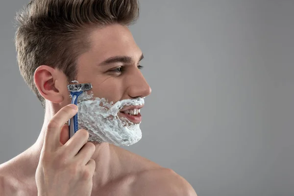Улыбающийся молодой человек бреется одноразовой бритвой — стоковое фото
