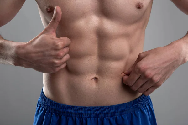 Young man demonstrating his six-pack abs and showing thumbs up — Stock Photo, Image