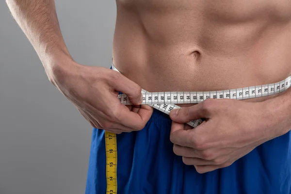 Young man with perfect abs measuring his waist