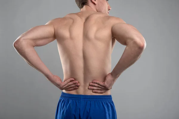 Young man with muscular body touching his lower back