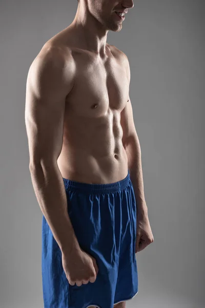 Sorridente giovane uomo con il corpo perfetto in piedi contro sfondo blu-grigio — Foto Stock