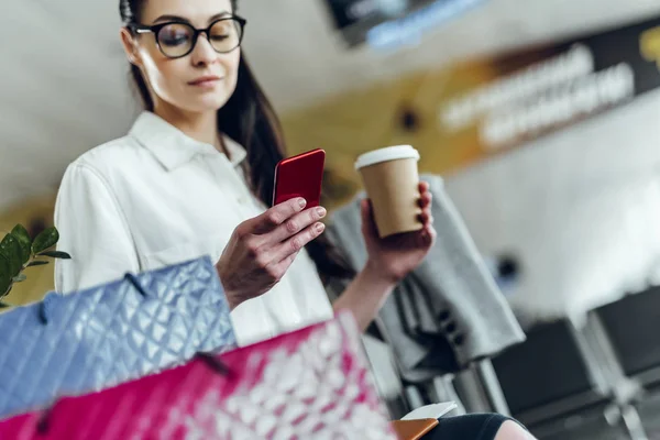 Mujer joven está tomando café y usando el teléfono en el aeropuerto — Foto de Stock