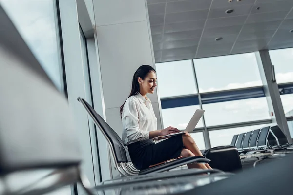 Mulher feliz é web-surf no laptop no aeroporto — Fotografia de Stock