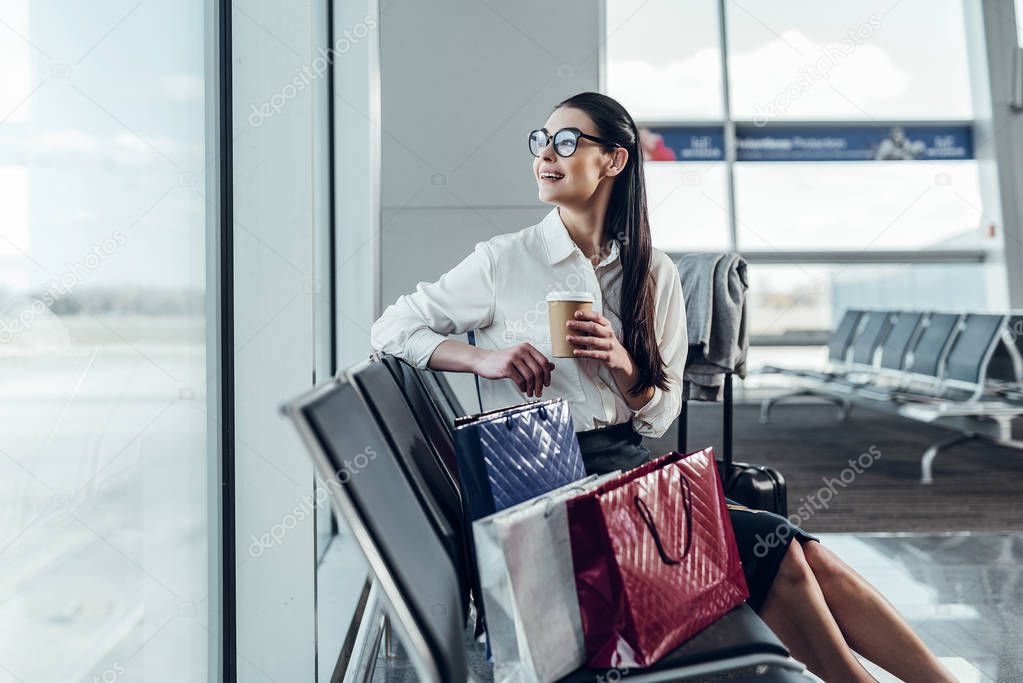 Happy young woman is enjoying hot drink in airport