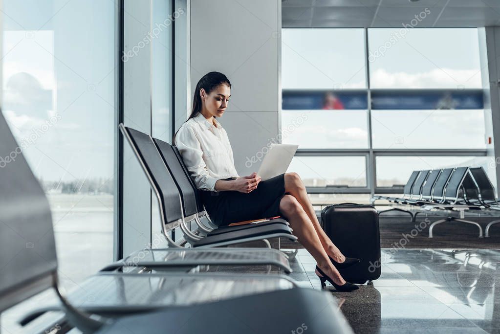 Calm businesswoman is waiting for departure with laptop