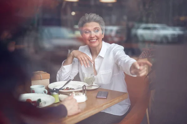 Ευτυχισμένη ηλικιωμένη κυρία δείχνοντας έξω κάθεται στο καφέ — Φωτογραφία Αρχείου