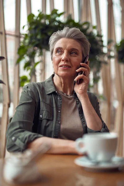 Стильна літня жінка розмовляє на мобільному телефоні в кафе — стокове фото