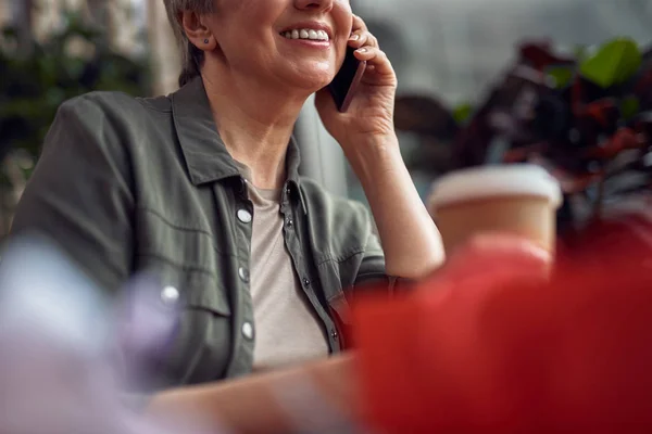 Cheerful aged woman talking by phone in cafe — Stock Photo, Image